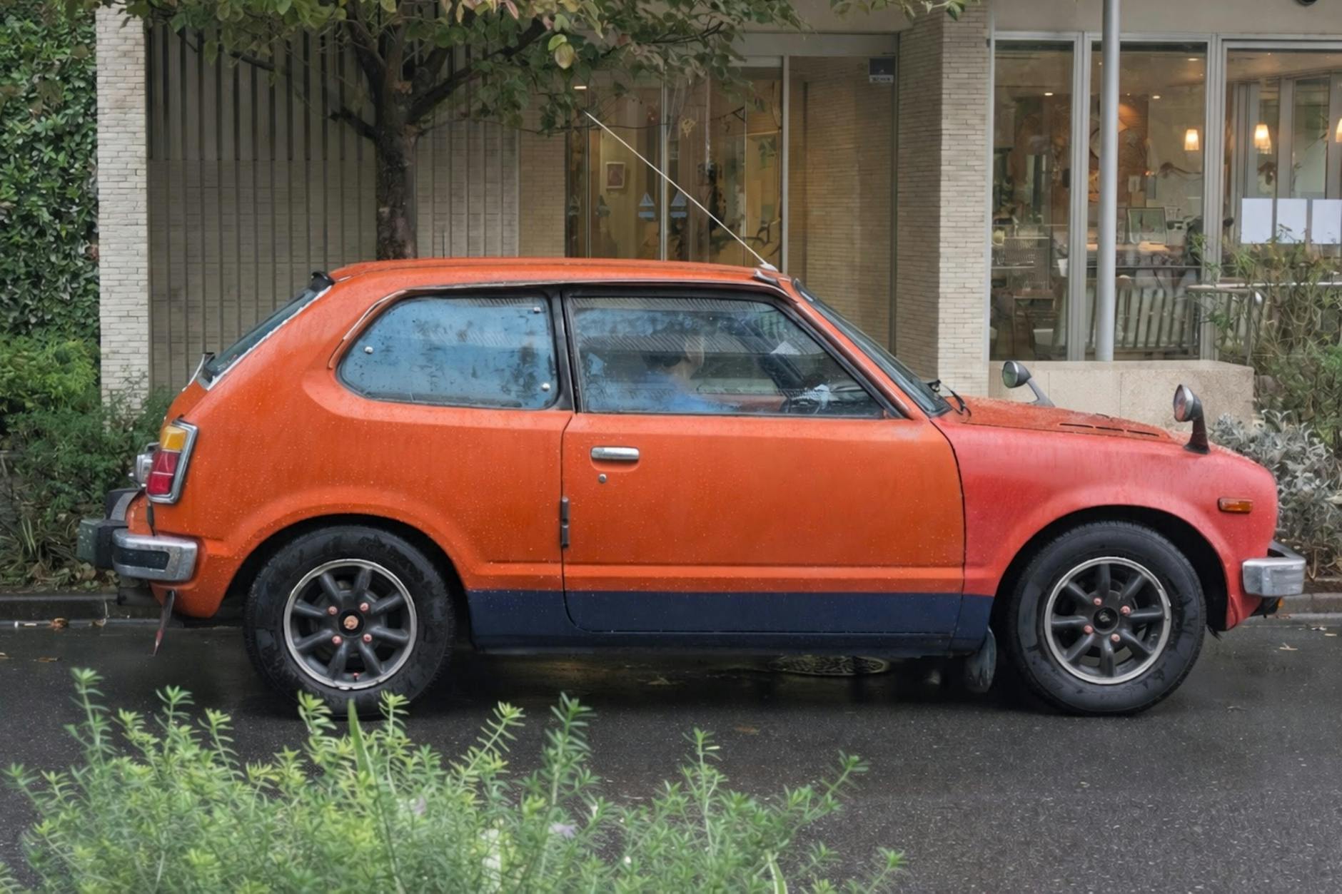 Pomarańczowy klasyczny hatchback na mokrej ulicy w Tokio