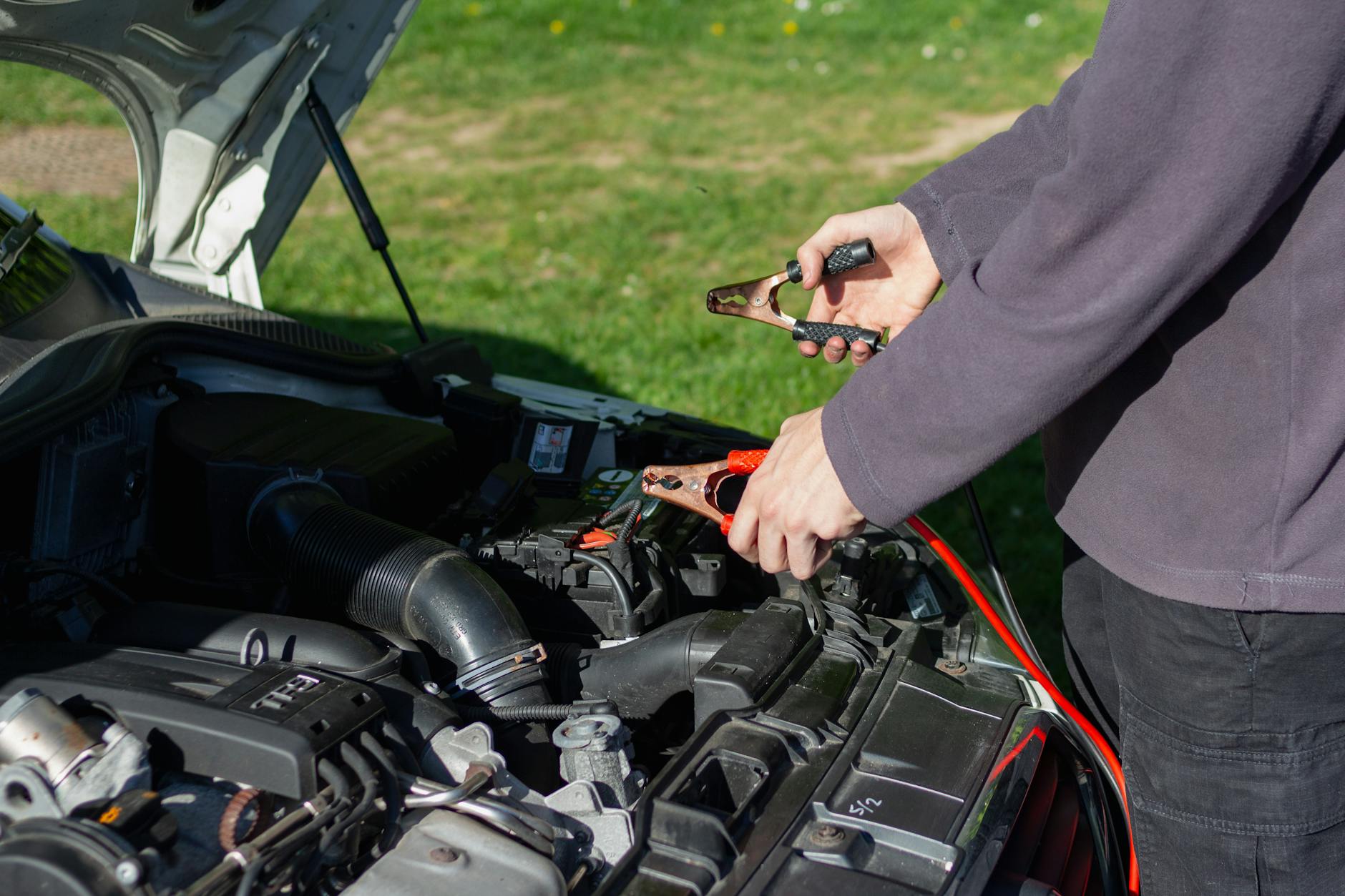 Mechanik na zewnątrz podpina kable rozruchowe do akumulatora auta